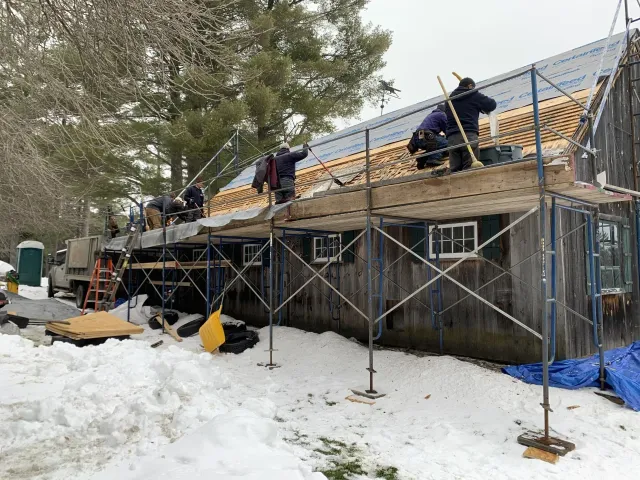 A group of men are working on the roof of a building in the snow.