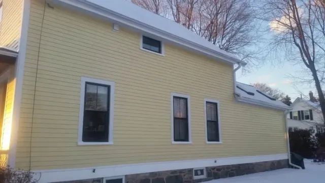 Yellow house exterior with white trim and snow on the roof in a winter neighborhood.