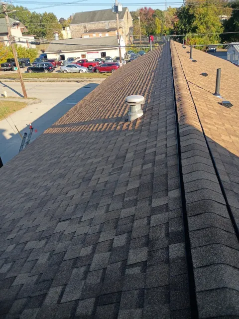 Rooftop with brown shingles and several vents, viewed from above on a sunny day.