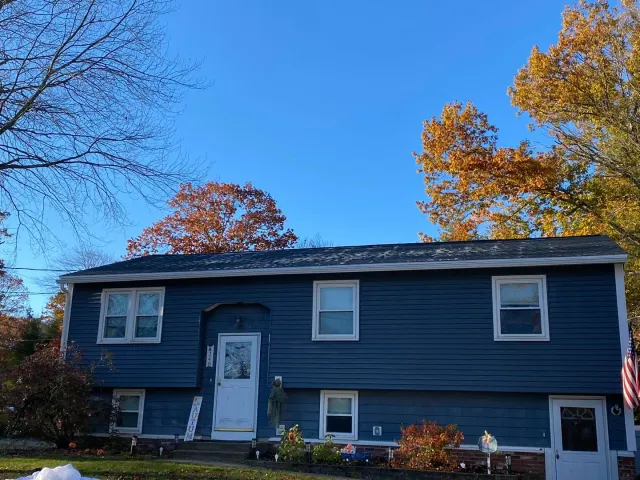 Two-story blue house with white trim. Autumn trees with orange leaves.
