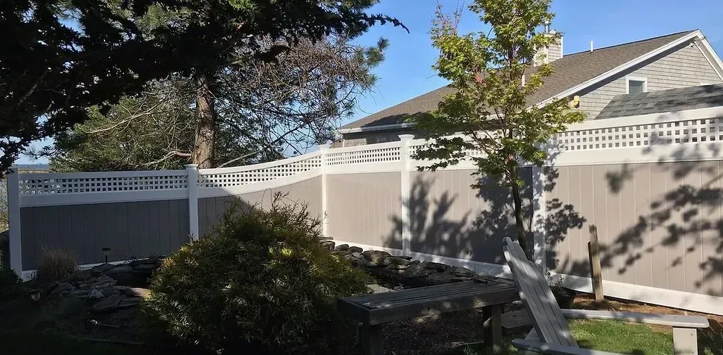 Backyard patio with white fence, gray shed, and trees in bright sunlight