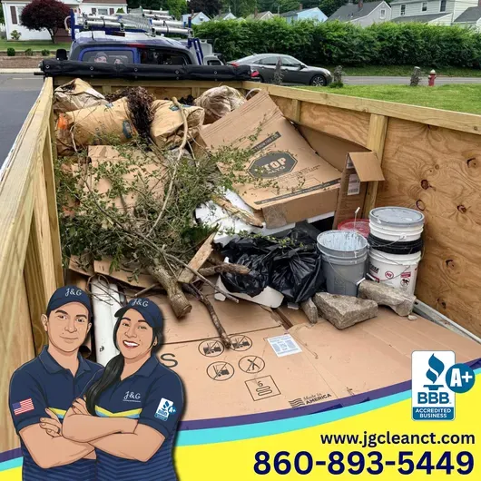 Dump trailer filled with cardboard, branches, and buckets on a residential street; JG Cleanout logo at bottom.