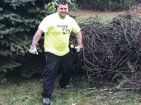 A Dump Guy employee smiling as he hauls away a large branch