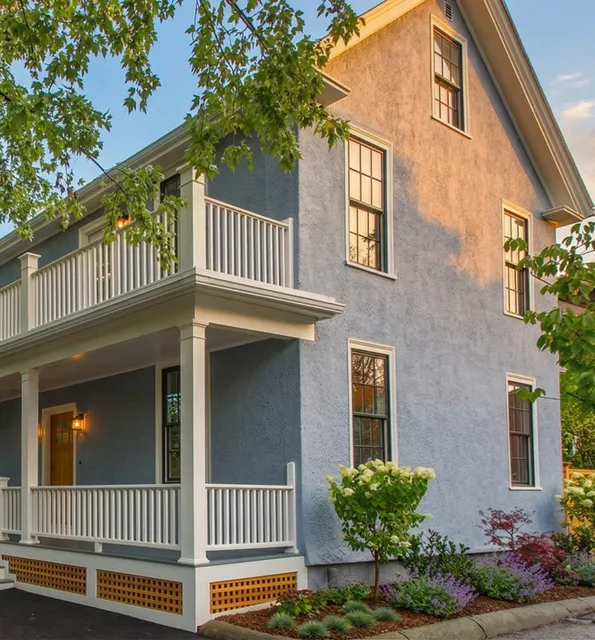 A two-story blue house with white trim at 17 Smith Place features a covered front porch, surrounded by landscaped plants and trees.