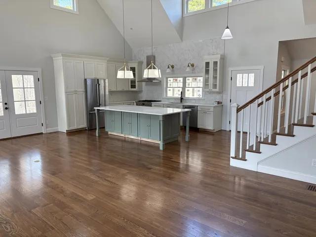 Vaulted great room with glossy refinished hardwood floor, open kitchen, and staircase