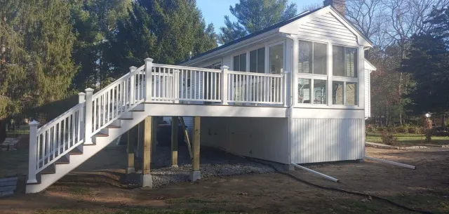 White deck and stairs leading to a sunroom with a clear, sunny sky.