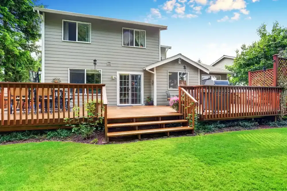 Large custom backyard wood deck with multiple entertaining areas, wide entry steps, and wood railings attached to a two-story home.