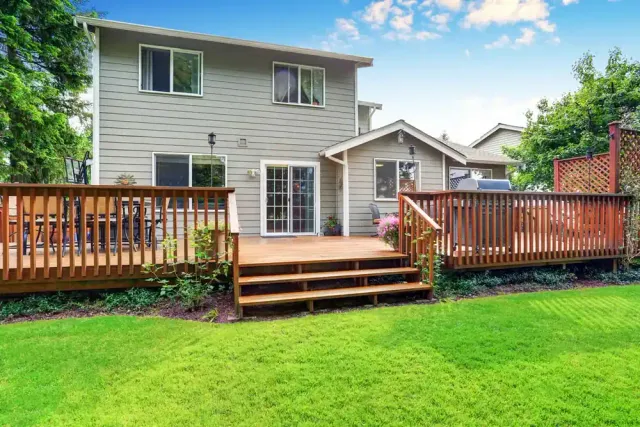 Large custom backyard wood deck with multiple entertaining areas, wide entry steps, and wood railings attached to a two-story home.