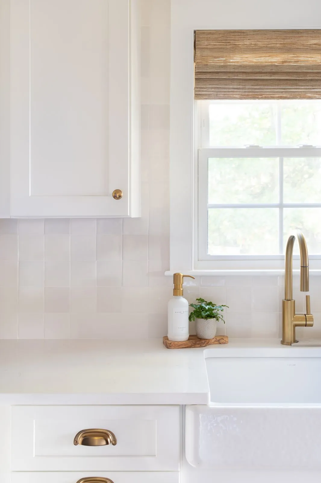 Indian Road kitchen sink detail with white zellige tile backsplash, farmhouse sink, brass faucet, and woven roman shade