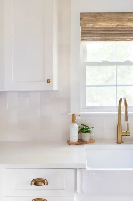 Indian Road kitchen sink detail with white zellige tile backsplash, farmhouse sink, brass faucet, and woven roman shade