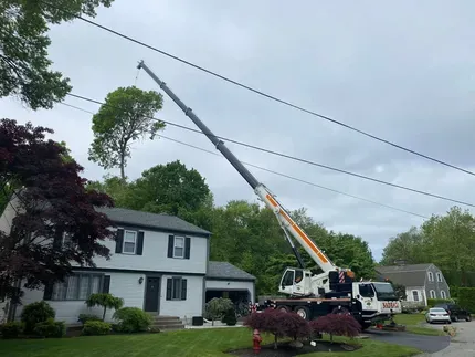 Crane truck lifting a long boom beside a house on a suburban street