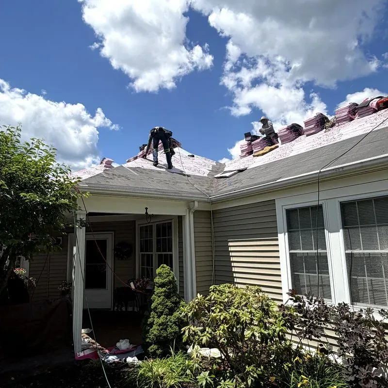 Crew finishing a shingle roof under summer sky