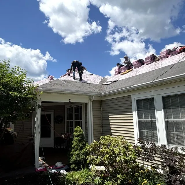 Crew finishing a shingle roof under summer sky