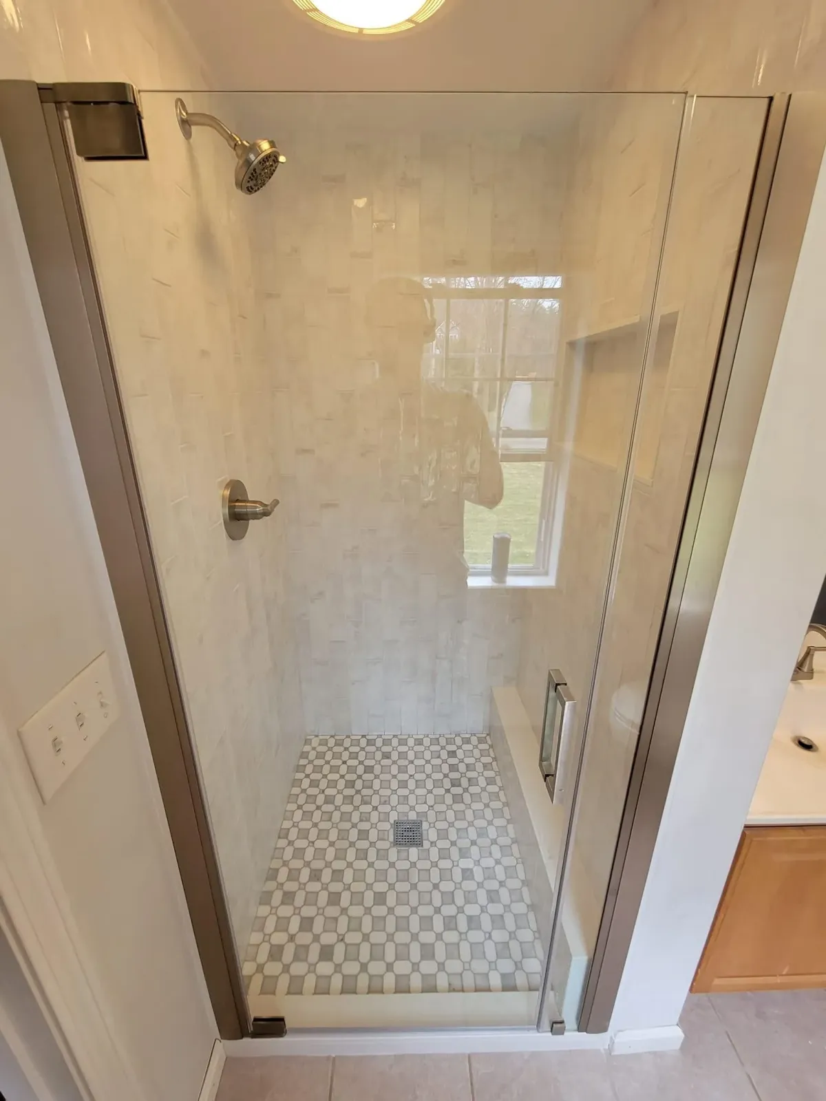 Empty glass shower stall with white tile floor and a wall-mounted showerhead in a bathroom.