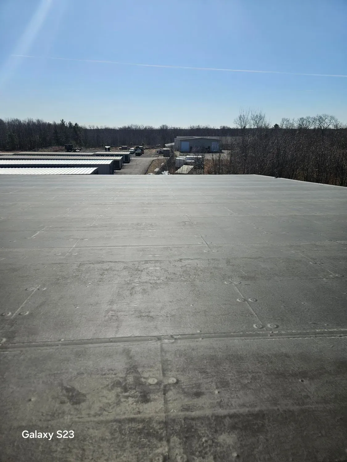 Flat, dark roof with a view of a distant road, buildings, and trees under a bright blue sky.