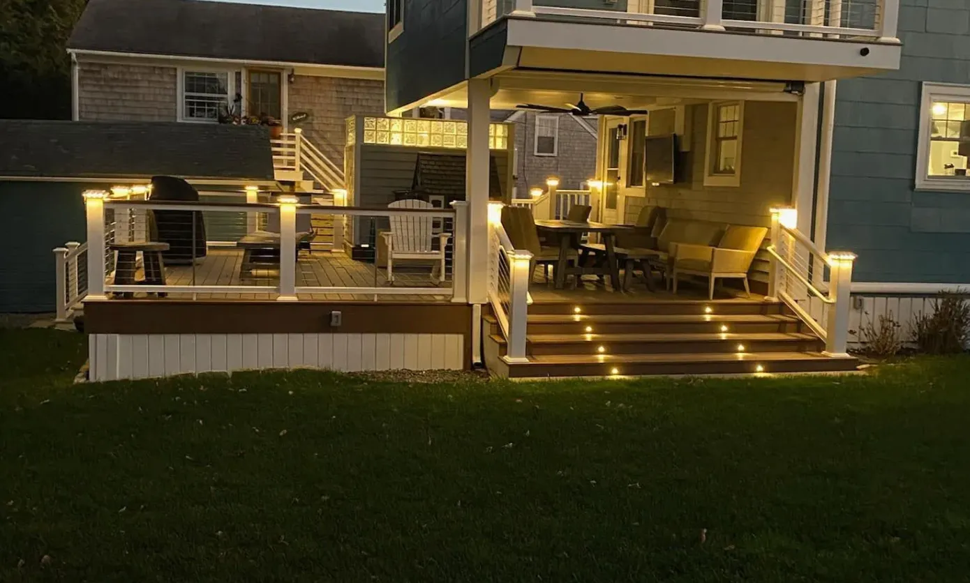 A lit outdoor deck with stairs, furniture, and string lights at dusk.