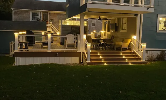 A lit outdoor deck with stairs, furniture, and string lights at dusk.