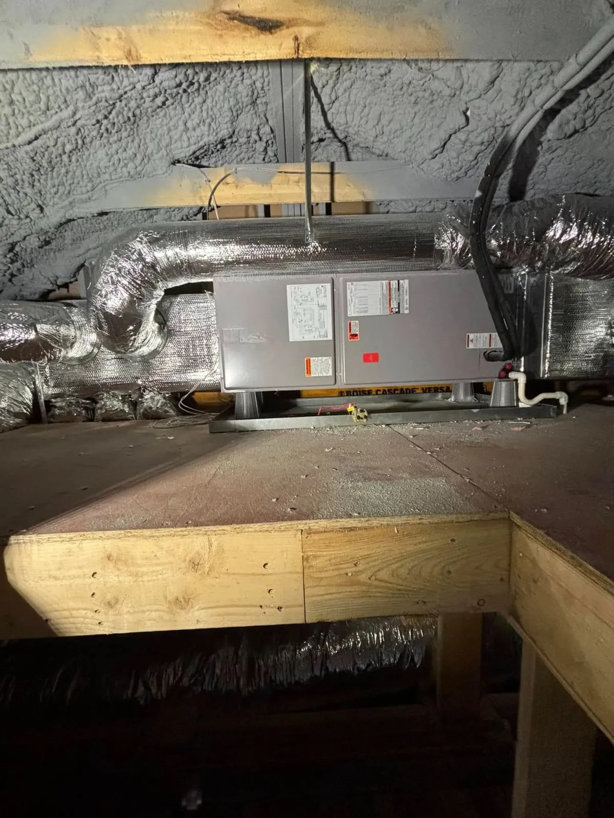 Metal HVAC equipment and ductwork in an attic crawl space beneath a wooden beam.