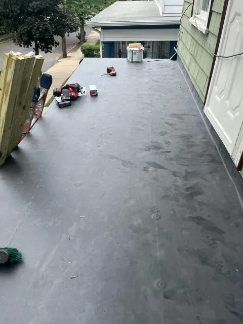 Flat black roof under construction with tools and a bucket near the far end, viewed from above