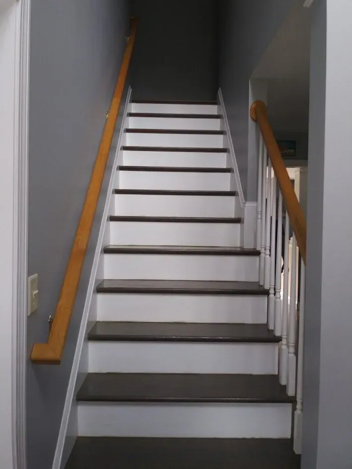 Indoor staircase with white steps, gray walls, and wooden handrails on both sides
