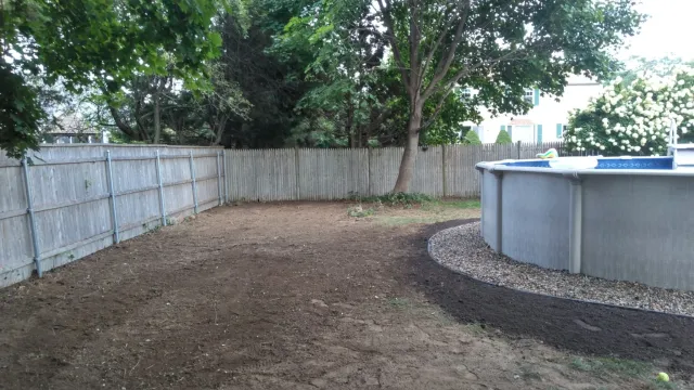 Backyard with above-ground pool, wooden fences, trees, and bushes.