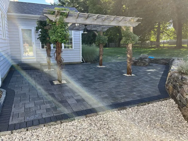 Backyard patio with gray pavers, pergola, and climbing vines beside a house