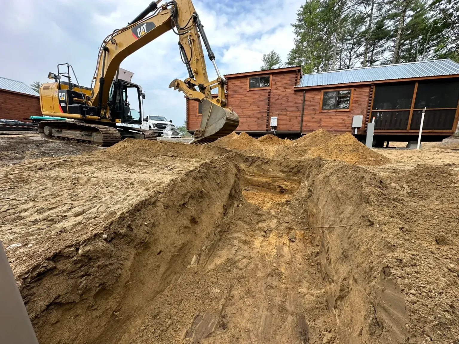 Excavator digging trench near cabin construction site
