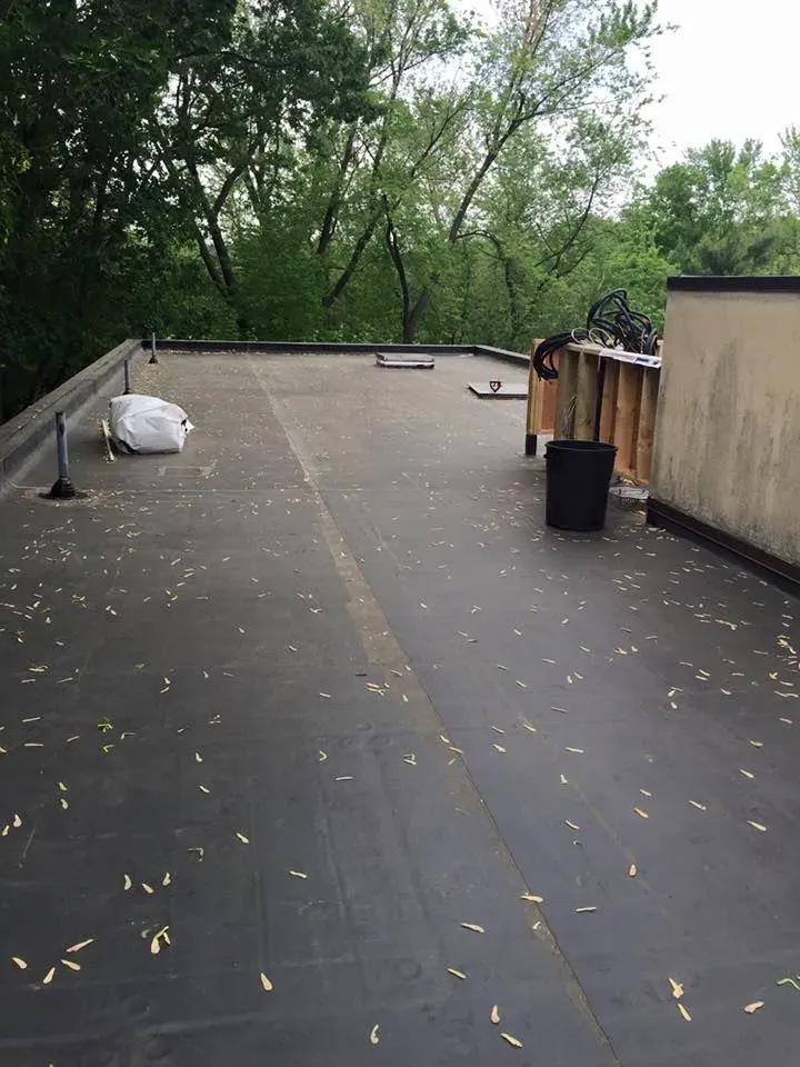 Black flat roof with scattered debris and trees in the background.
