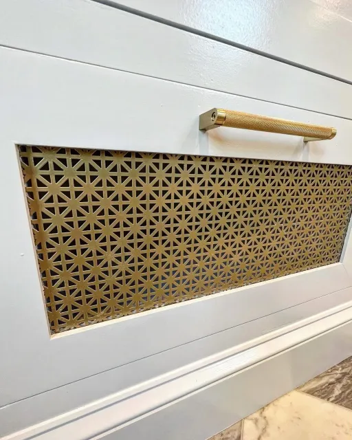 A white panel with a decorative gold grill inserting into it, and a gold handle above the grill.