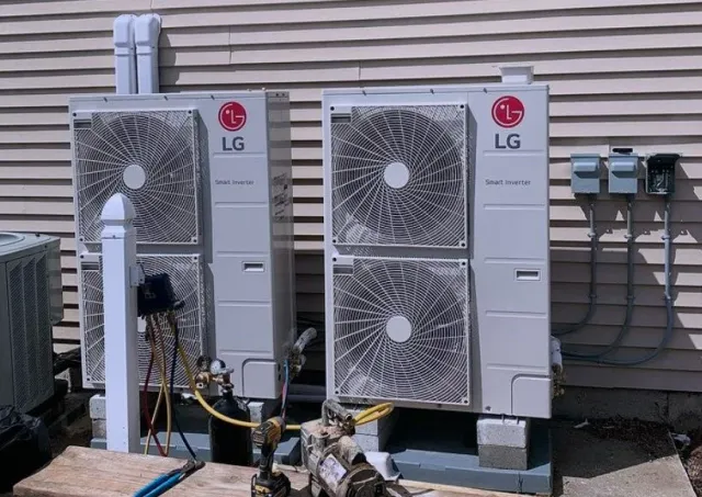 Two LG heat pump units with air filters, electrical wiring, and control panels outside a house with beige siding.