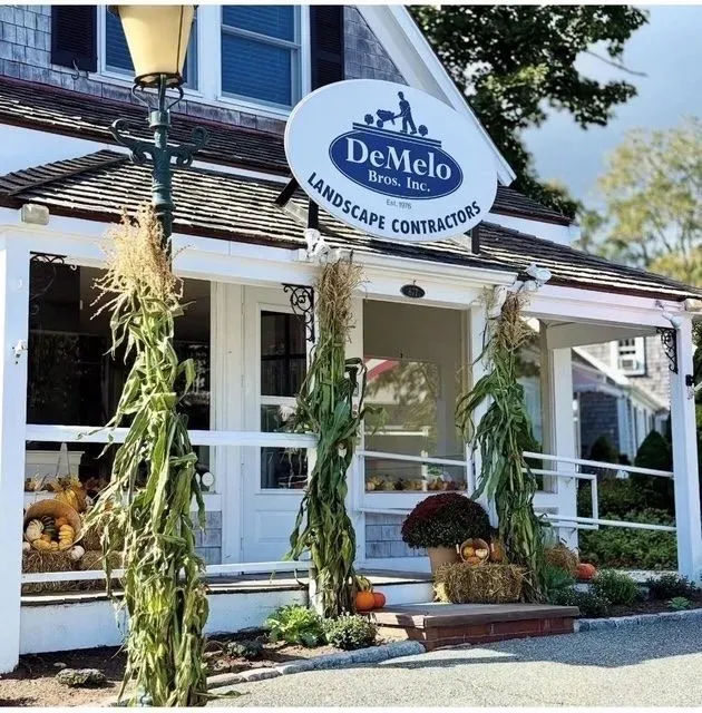 DeMelo Landscape Contractors storefront with white porch, hanging plants, and garden displays