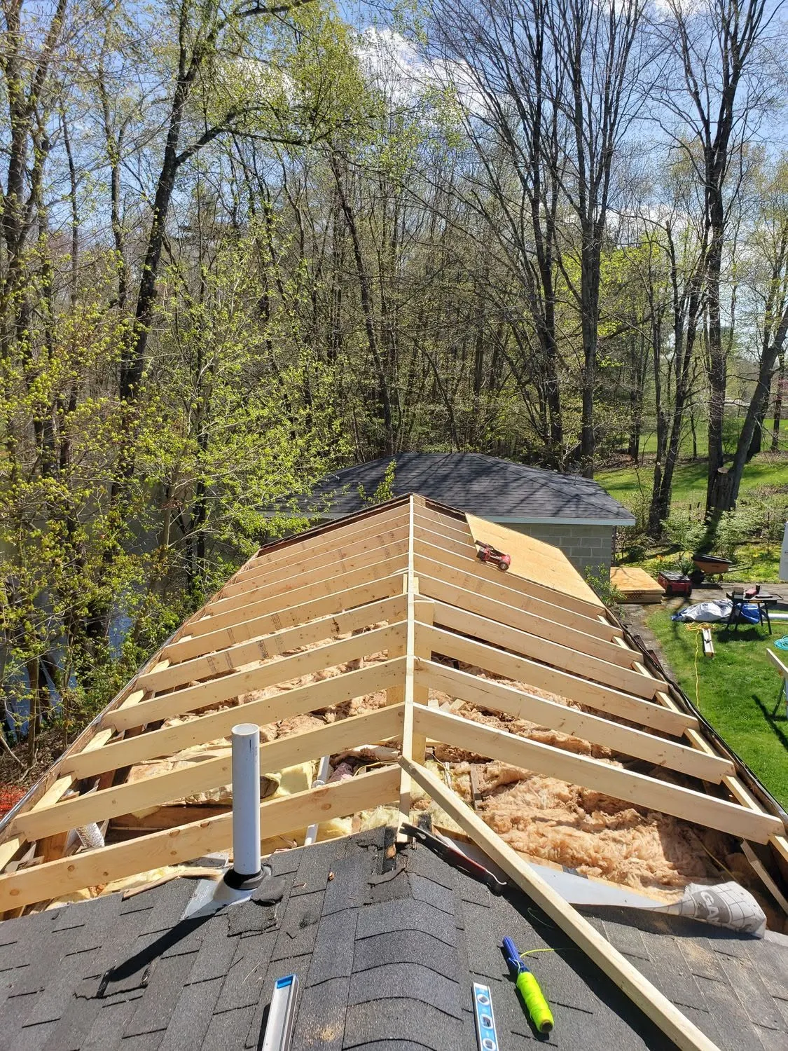 Roof framing construction with wooden trusses and insulation in wooded residential area