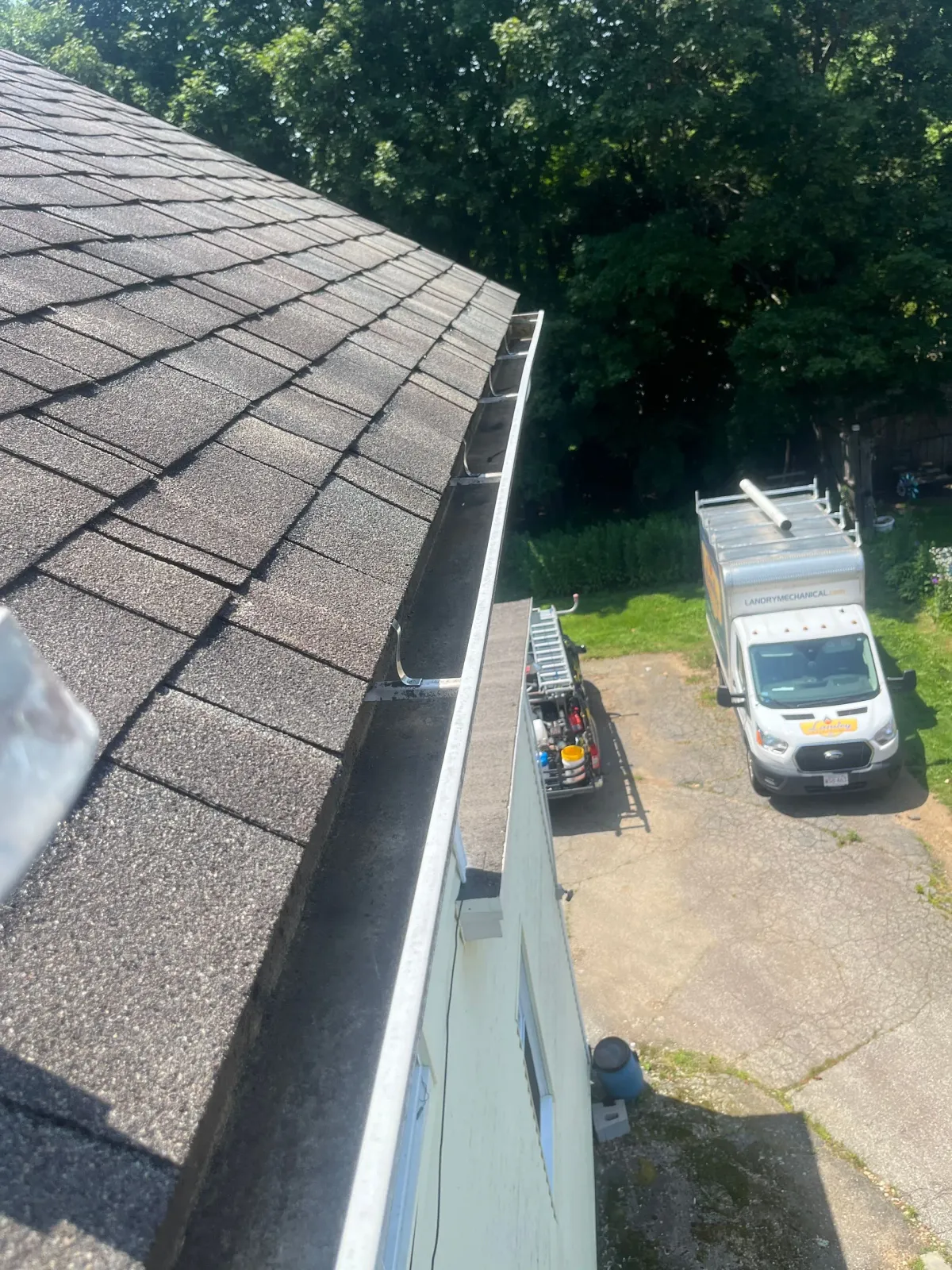 View from a roof edge onto a driveway with a white utility truck and landscaping equipment below