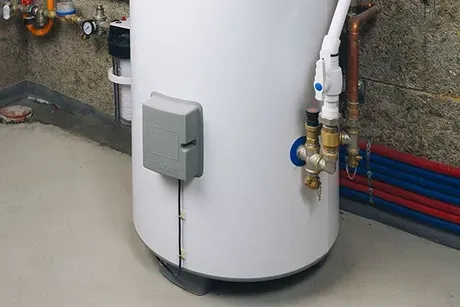 A white water heater is sitting in a basement next to pipes.