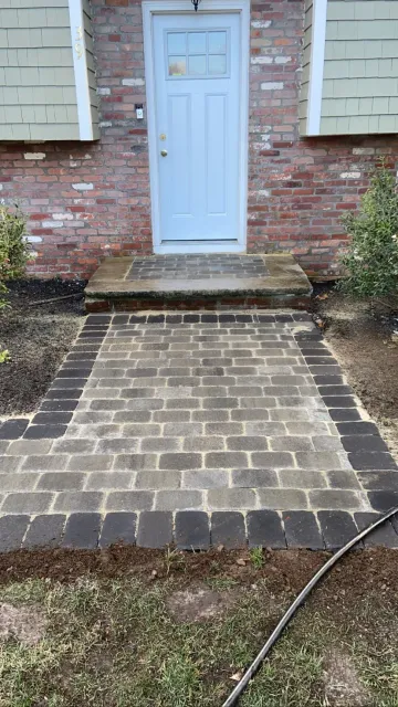 Brick walkway leading to a blue door, flanked by bushes and a brick house.