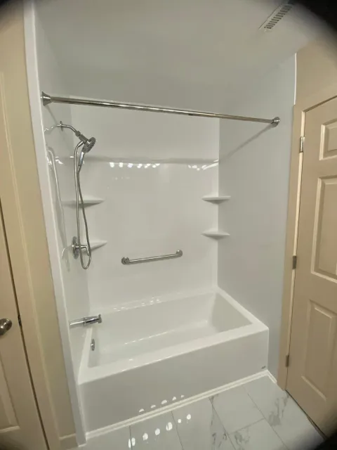 Empty white bathtub with a showerhead and silver grab bars inside a bathroom corner.