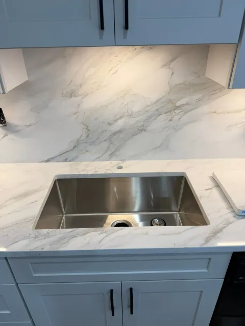 Kitchen countertop with white marble-look surface and stainless steel sink, surrounded by blue cabinets