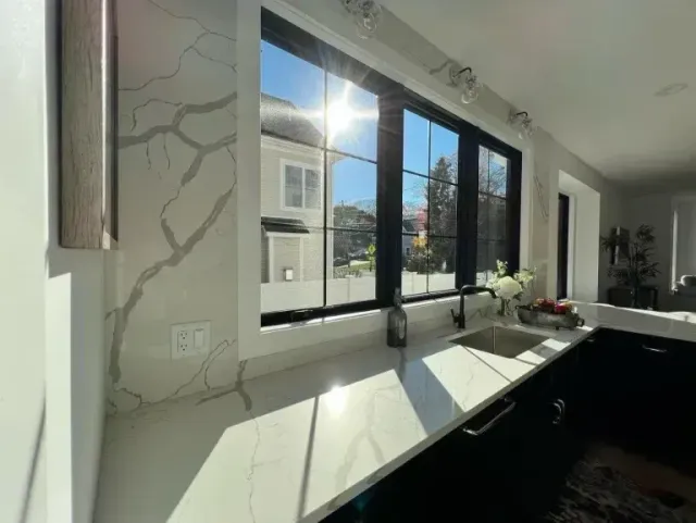 Bright modern kitchen with black-framed windows, white countertop, and sunlight streaming in.