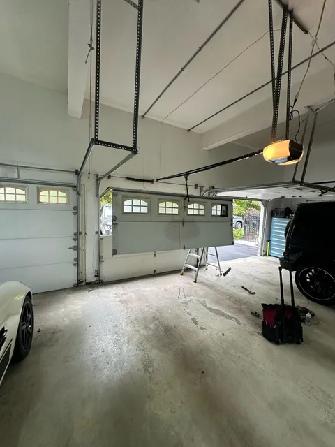 White garage door in front of harage doors with rails of garage door openers and a cement floor.