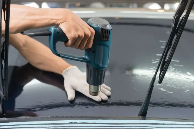 Person using a heat gun to apply tint to a car window.