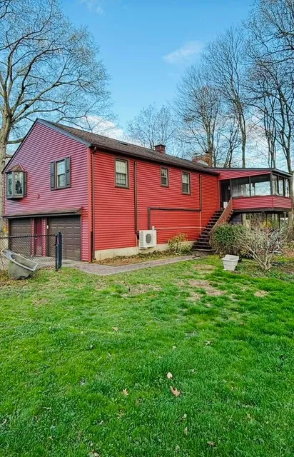 Red two-story house with a metal roof in a grassy yard, surrounded by bare trees and blue sky