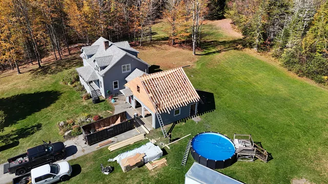 Roofing crew installing shingles on new construction garage addition in Stowe Vermont — aerial fall foliage