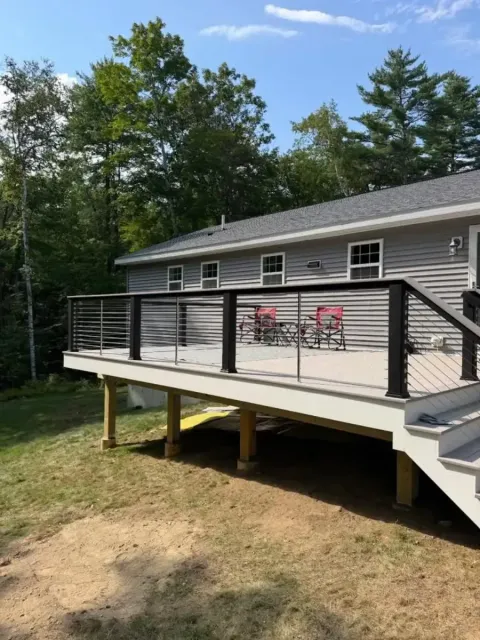 House with elevated deck and railing, two red chairs on the porch, surrounded by trees