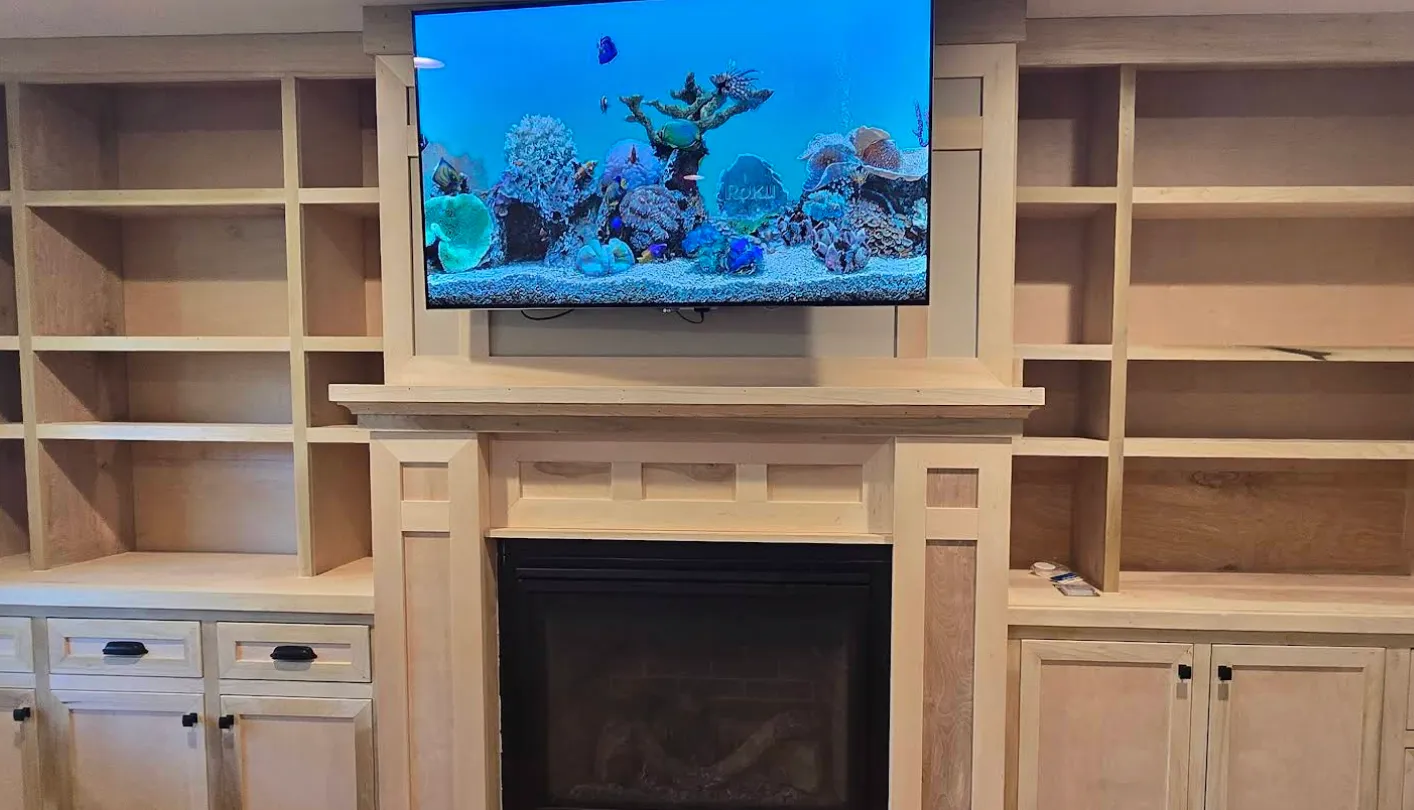 Wooden built-in shelves and cabinets surrounding a fireplace with a TV mounted above it, displaying an underwater coral reef scene.