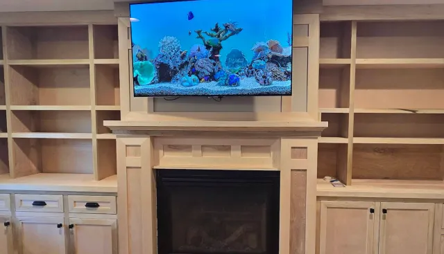 Wooden built-in shelves and cabinets surrounding a fireplace with a TV mounted above it, displaying an underwater coral reef scene.
