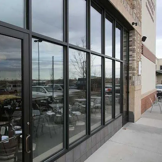 Exterior view of a storefront with large glass windows reflecting parked cars and a cloudy sky.