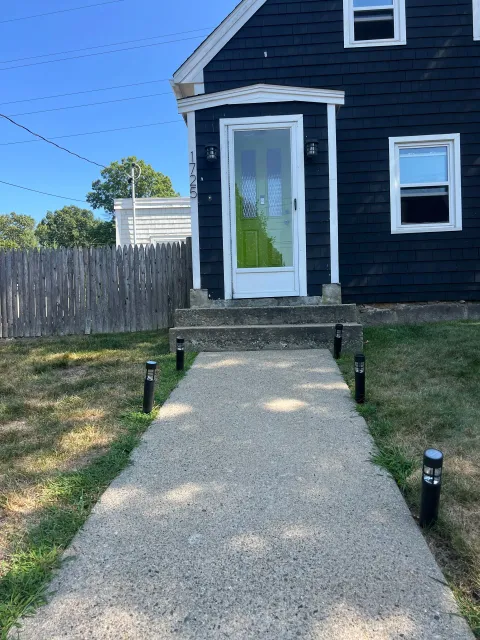 A dark-painted house with a concrete walkway leading to the front door, lined with small black lights
