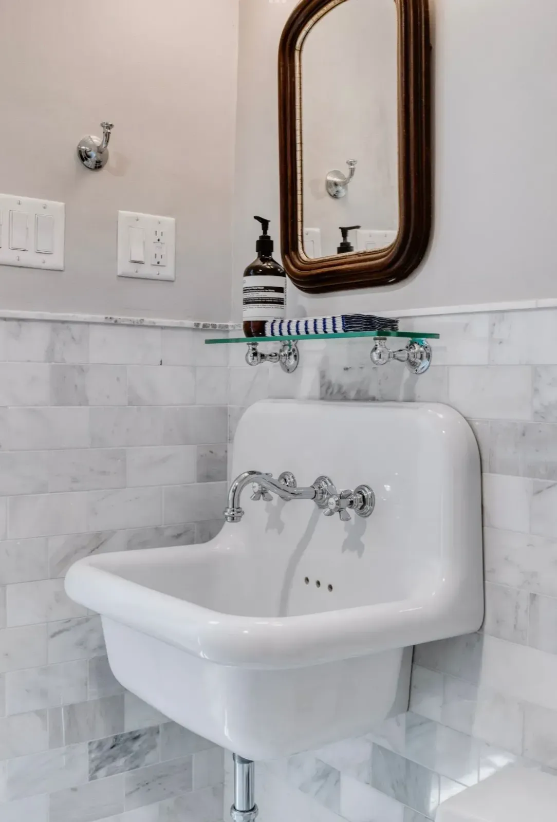 White wall-mounted bathroom sink with chrome faucet, soap dispenser, and mirror above marble-look tile.