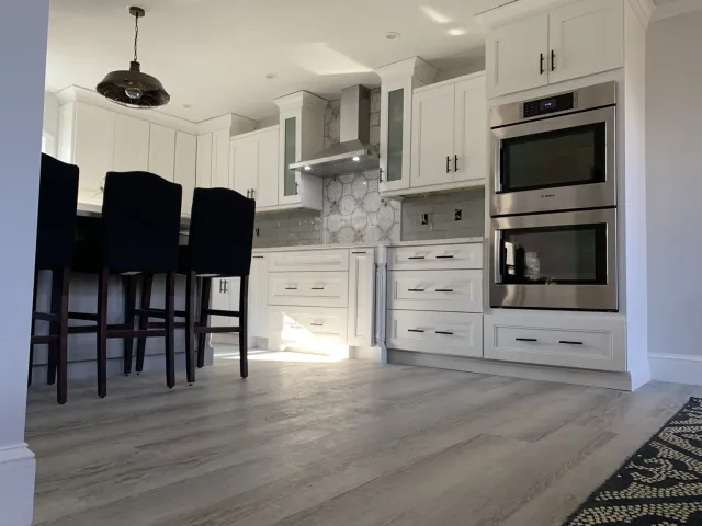 White custom kitchen with island, built-in ovens and tile backsplash