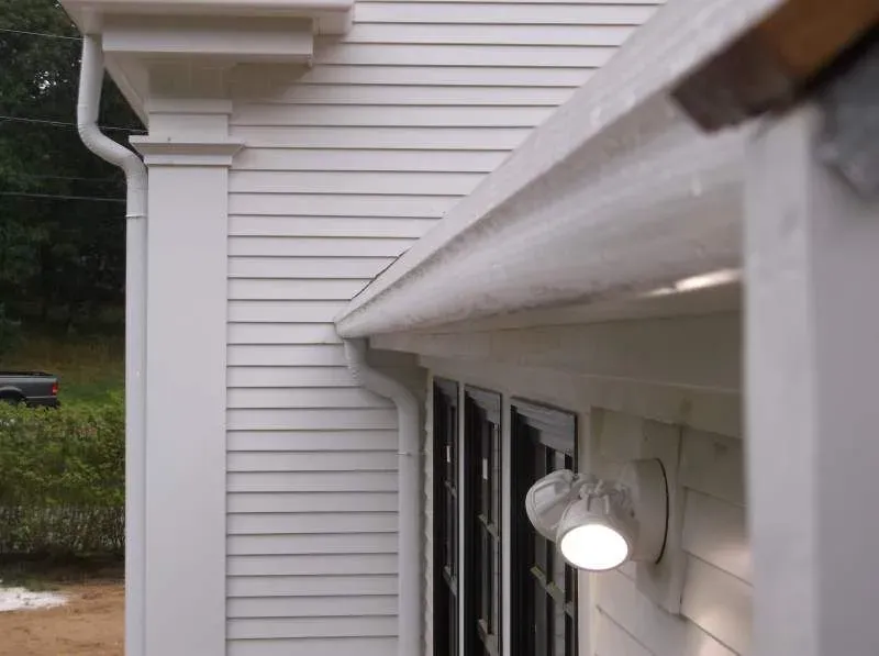 White house exterior with column, gutter, and a lit security light.